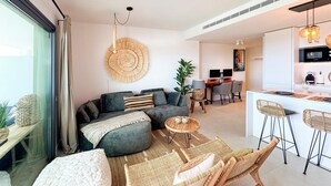 Una sala de estar moderna con un sofá gris, un tapiz redondo tejido, una zona de comedor con barra y una cocina con microondas.