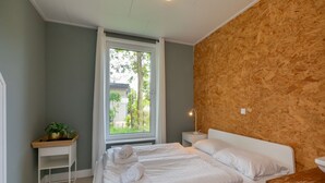 A bedroom with a bed, a bedside table, a nightstand, a window, and a view of the outdoors.