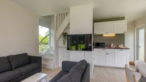 A modern living room with a grey sofa and a white coffee table, a kitchen with white cabinets and a flat-screen TV, and a staircase leading to another level.