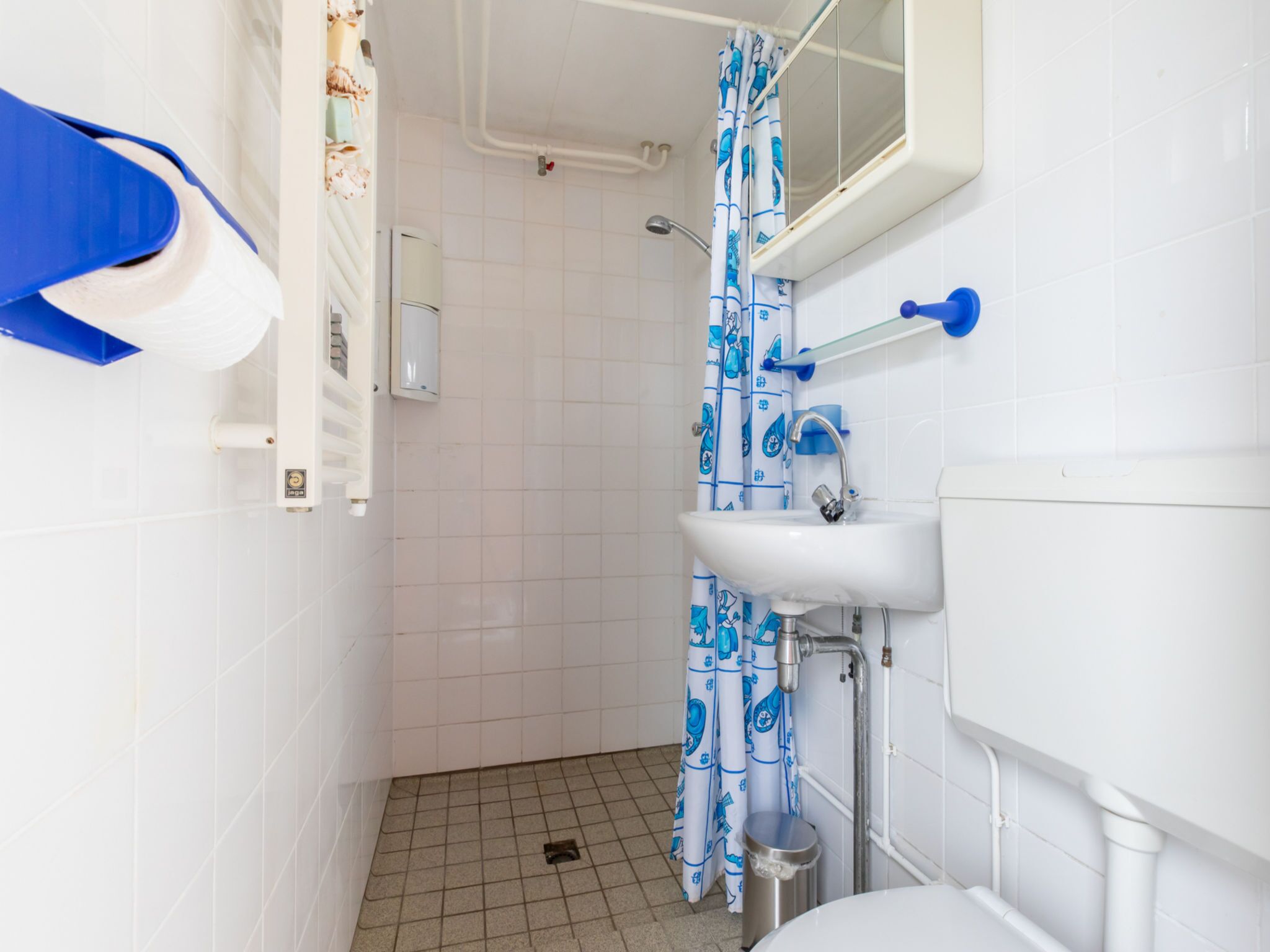 A small bathroom with a white sink, a blue faucet, a white toilet, and a shower curtain with a blue pattern.