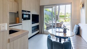 Uma cozinha moderna com eletrodomésticos embutidos, um espaço de jantar com mesa redonda e cadeiras, e uma porta de vidro deslizante que dá para um pátio externo.
