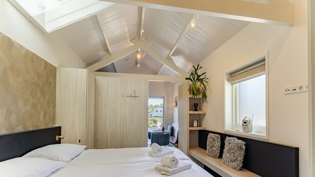 Quarto com claraboia, uma cama, mesa de cabeceira com rádio e vista para o exterior.
