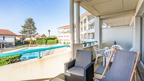 Un balcón con vista a la piscina, mobiliario de mimbre y una vista de zona residencial.