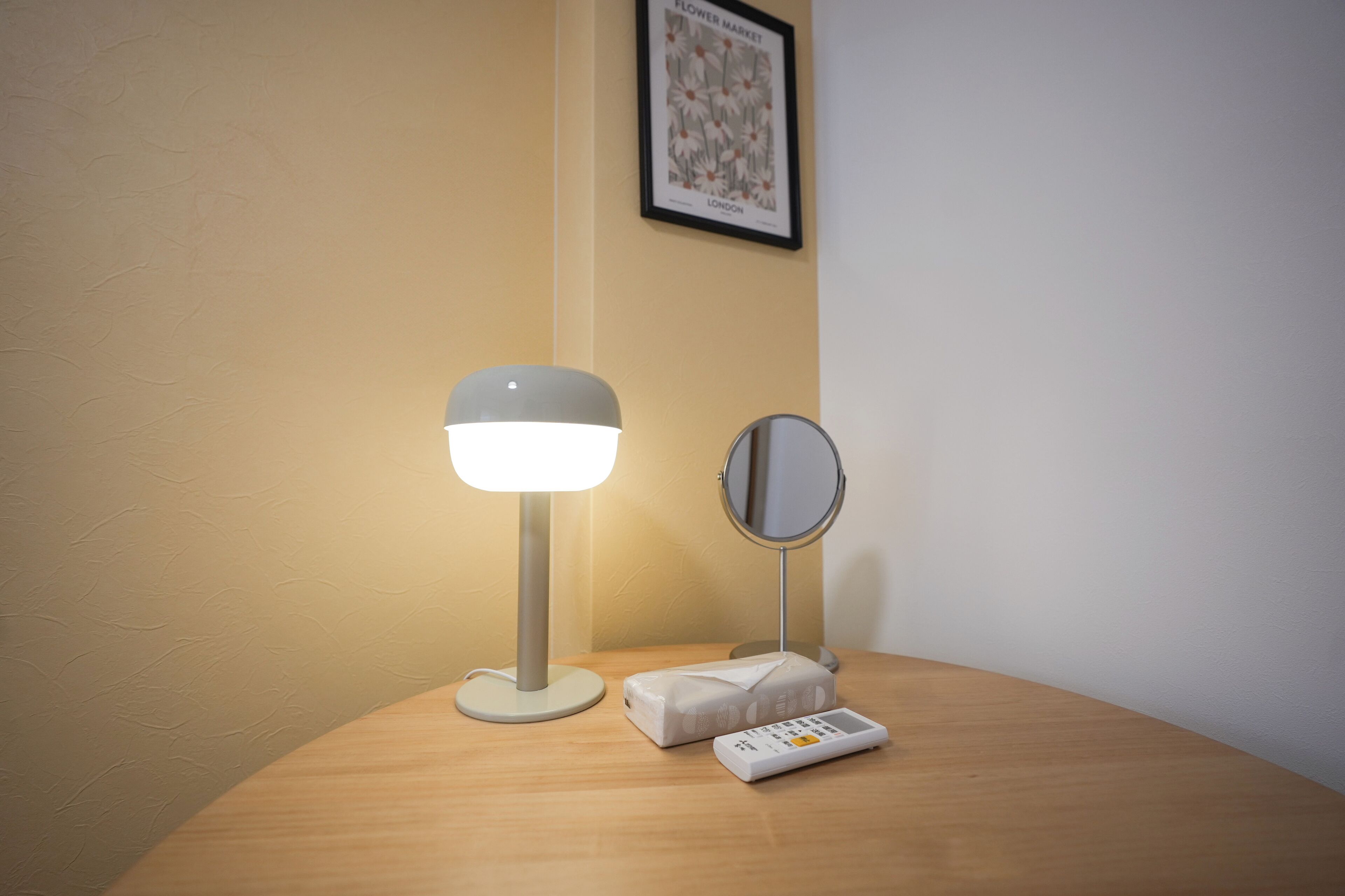 Uma mesa de cabeceira com uma luminária, um controle remoto e um espelho.