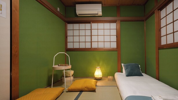 A traditional Japanese-style room with tatami flooring, a futon bed, a shoji screen, and a small table with a lamp. - Otabiya Noda (Osaka)