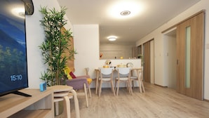 A modern living room with a flat-screen TV, wooden furniture, a large plant, and a dining area with chairs and a table. - Otabiya Noda (Osaka)