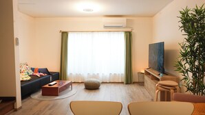A living room with a sofa, a coffee table, a TV, and a large plant. - Otabiya Noda (Osaka)