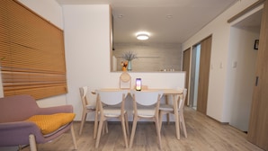 A modern dining area with a wooden table and chairs, a purple sofa with a yellow cushion, and a large mirror above the table. - Otabiya Noda (Osaka)