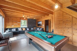 A wooden interior with a pool table, sofa, and a view of the outdoors.