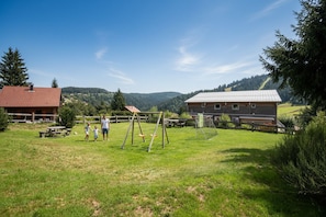 A grassy outdoor area with a swing set, picnic tables, and a building with a red roof.
