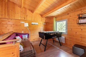 A cozy room with wooden walls, a futon bed, a foosball table, and a window with a view.