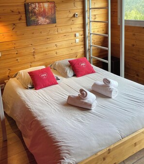 A wooden-paneled room with a bed, two red pillows, and a painting on the wall.
