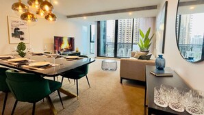 A modern dining area with a long table, green chairs, and hanging pendant lights.