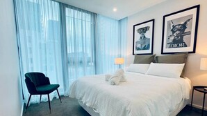 A hotel room with a large bed, a chair, a window with sheer curtains, and two framed posters on the wall.