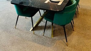 A dining area with a black marble table, green upholstered chairs, and a modern chandelier.
