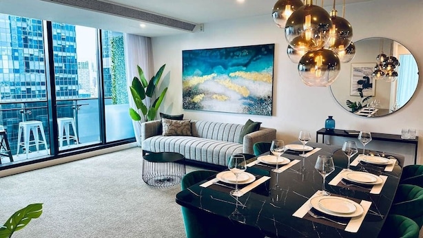 A modern dining area with a black marble table set for six, a striped sofa, and a large abstract painting on the wall.