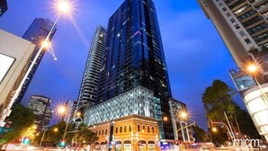 A modern high-rise building with a glass facade, surrounded by other tall buildings and streetlights.