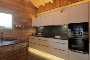 A modern kitchen with wooden walls, a built-in oven, and a window. - ✨ Chalet Zen Altitude – Luxury Chalet with Hot Tub, Sauna (Gérardmer)