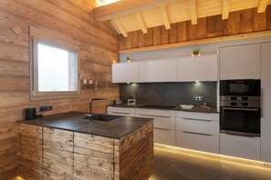 A modern kitchen with wooden paneling, a central island, and built-in appliances. - ✨ Chalet Zen Altitude – Luxury Chalet with Hot Tub, Sauna (Gérardmer)