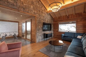 A modern interior with a stone wall, wooden ceiling, a television, a sofa, and a table. - ✨ Chalet Zen Altitude – Luxury Chalet with Hot Tub, Sauna (Gérardmer)