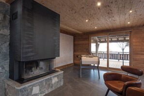 A modern interior with a stone fireplace, wooden ceiling, and a view to an outdoor deck. - ✨ Chalet Zen Altitude – Luxury Chalet with Hot Tub, Sauna (Gérardmer)
