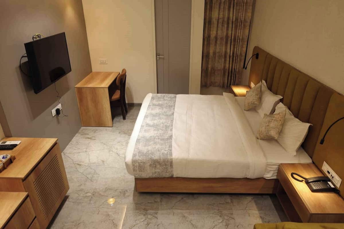 A hotel room with a large bed, bedside tables, a desk, a television, and a door.