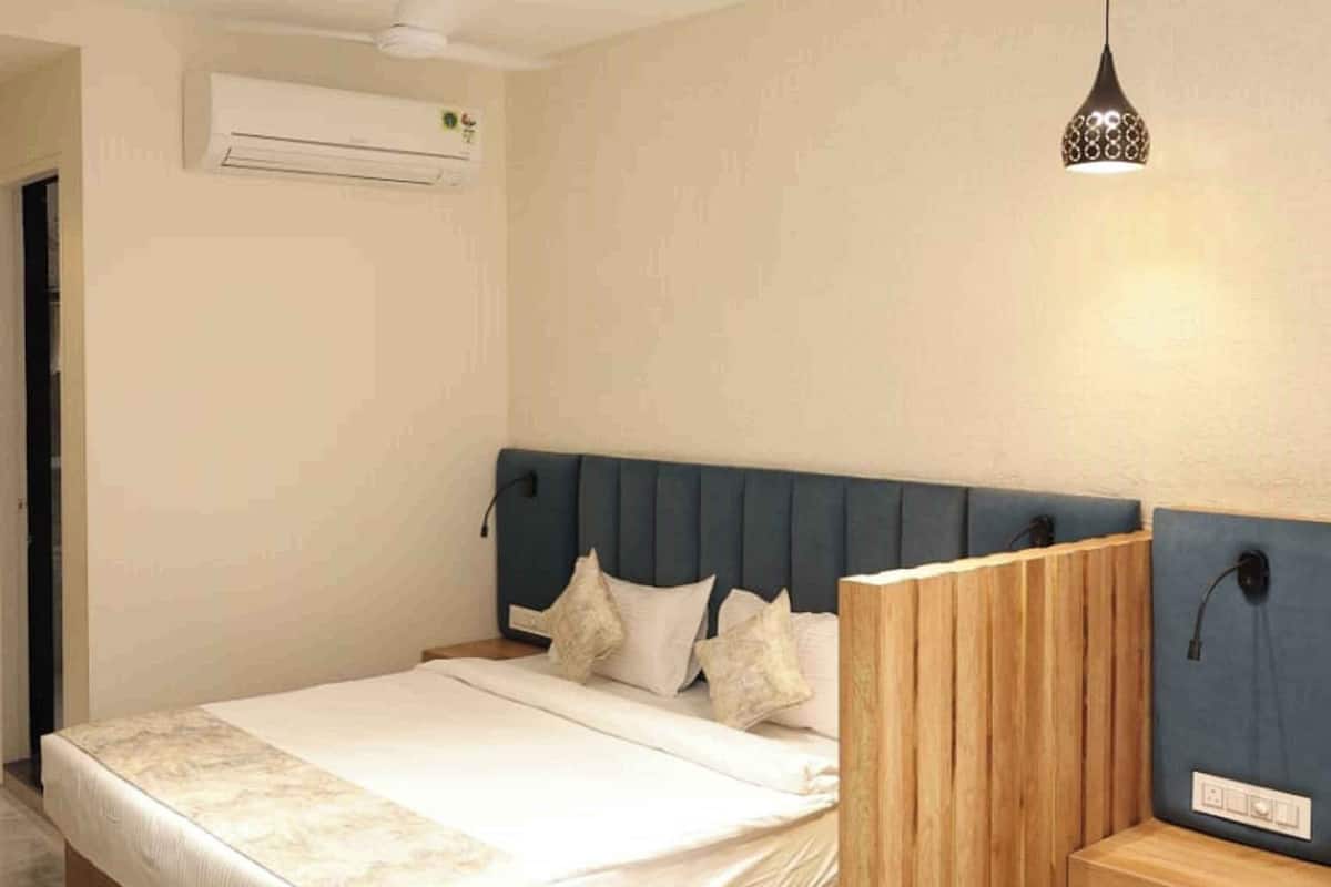 A modern bedroom with a wooden headboard, a large bed, an air conditioning unit, and a pendant light.