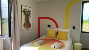 Een slaapkamer met een bed, een raam, een kunstwerk aan de muur en een nachtkastje.