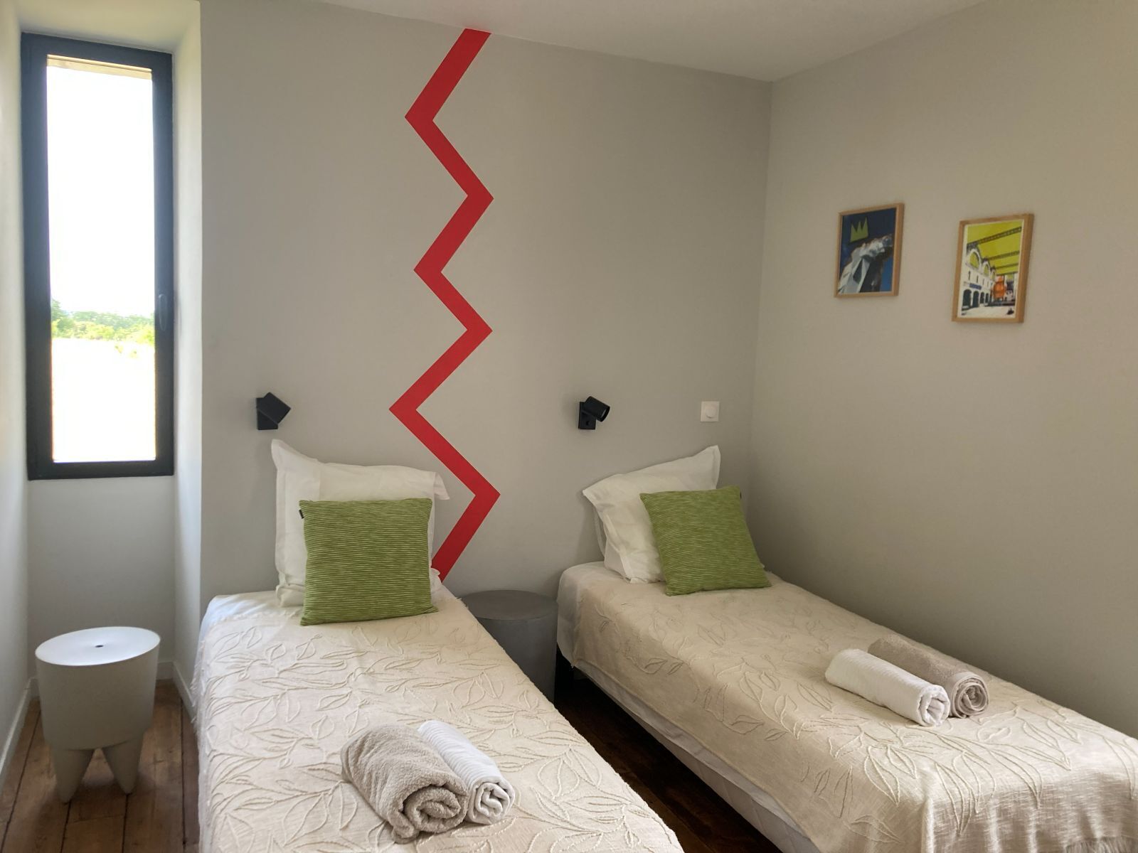 A room with two beds, a window, and a red zigzag wall design.