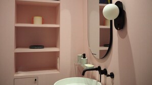 Un baño con lavamanos blanco, espejo y repisas con artículos de tocador.