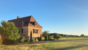 Una casa de dos pisos con techo inclinado, rodeada por un campo cubierto de césped y árboles.