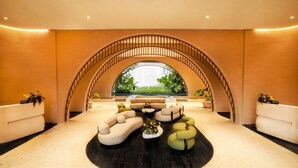 A spacious lobby with a central seating area, a reception desk, and a large arched window overlooking greenery. - Noema Resort Pererenan Bali (Pererenan)