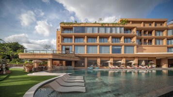 A modern hotel with a large pool, multiple balconies, and outdoor seating areas.