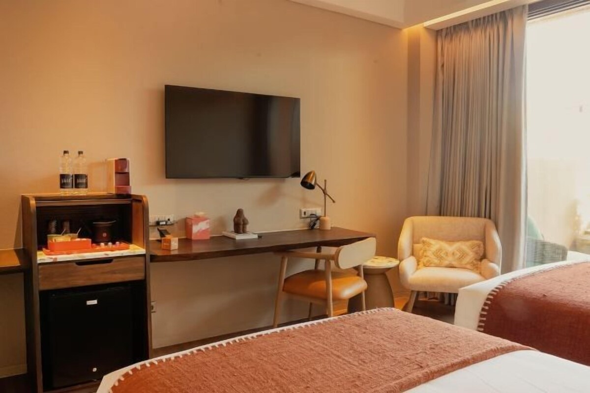 Habitación de hotel con cama, escritorio, silla, televisión y ventana con cortinas.