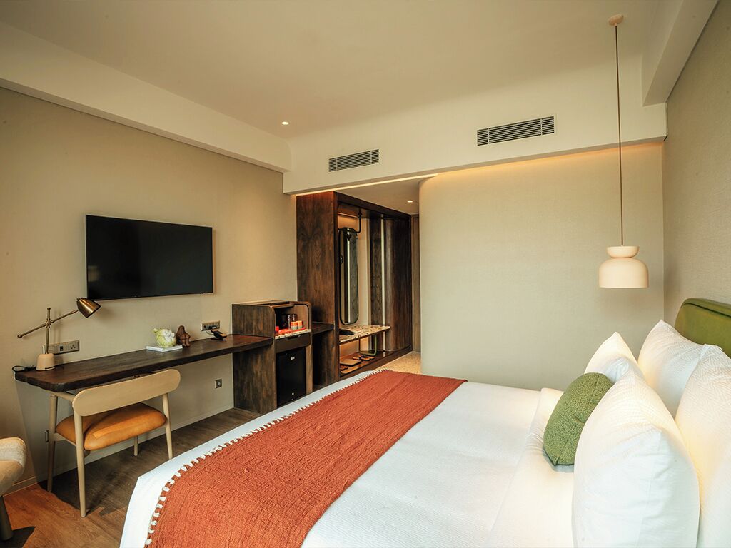 A modern hotel room with a large bed, a desk, a flat-screen TV, and a separate seating area.