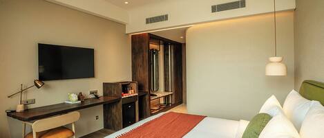 A modern hotel room with a large bed, a desk, a flat-screen TV, and a separate seating area.