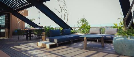 A rooftop terrace with a wooden deck, a sofa set, a round table, and potted plants.