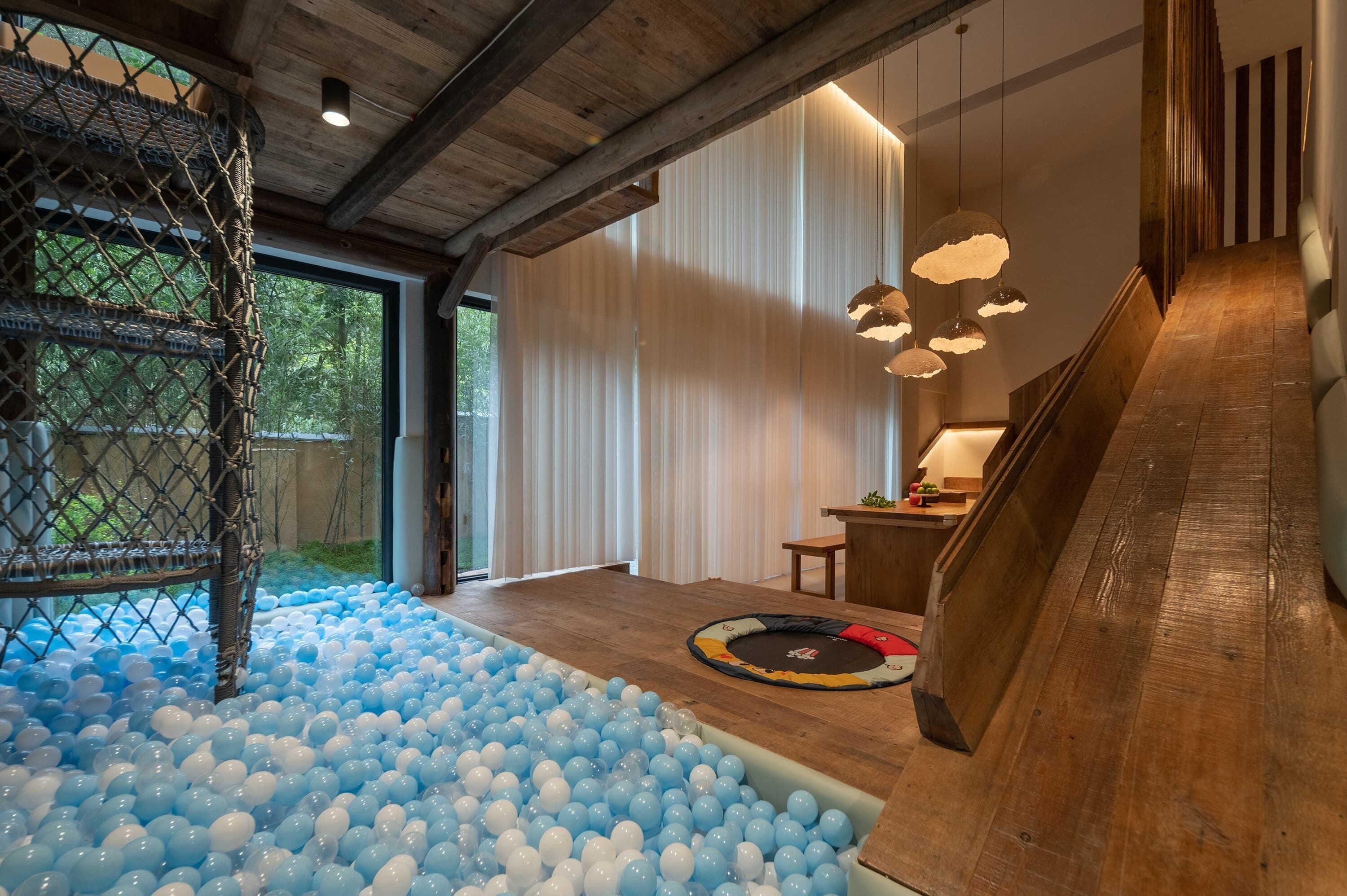 A room with a ball pit, a wooden slide, and a netted play area.