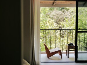 Ein Balkon mit einem Holzstuhl und einem kleinen Tisch, mit Blick auf einen Garten mit Bäumen und einem Zaun.