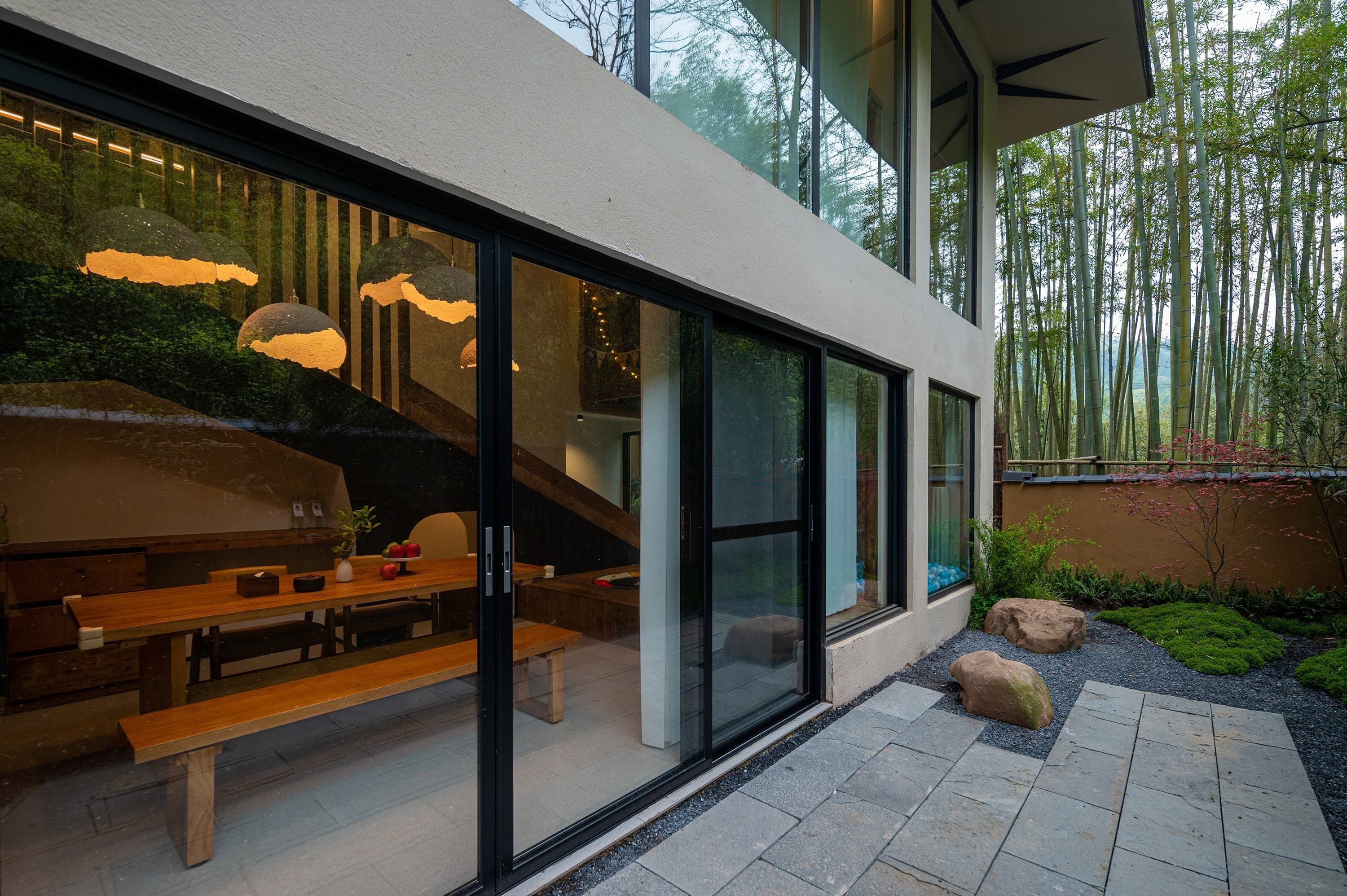A modern house with large glass windows, a wooden bench, and a stone pathway.