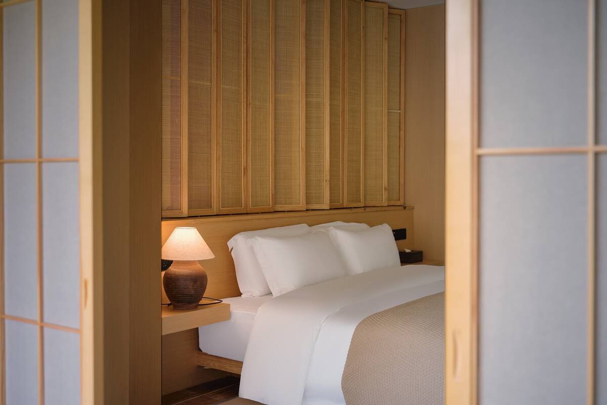 A hotel room with a bed, a nightstand with a lamp, and a traditional Japanese shoji screen.