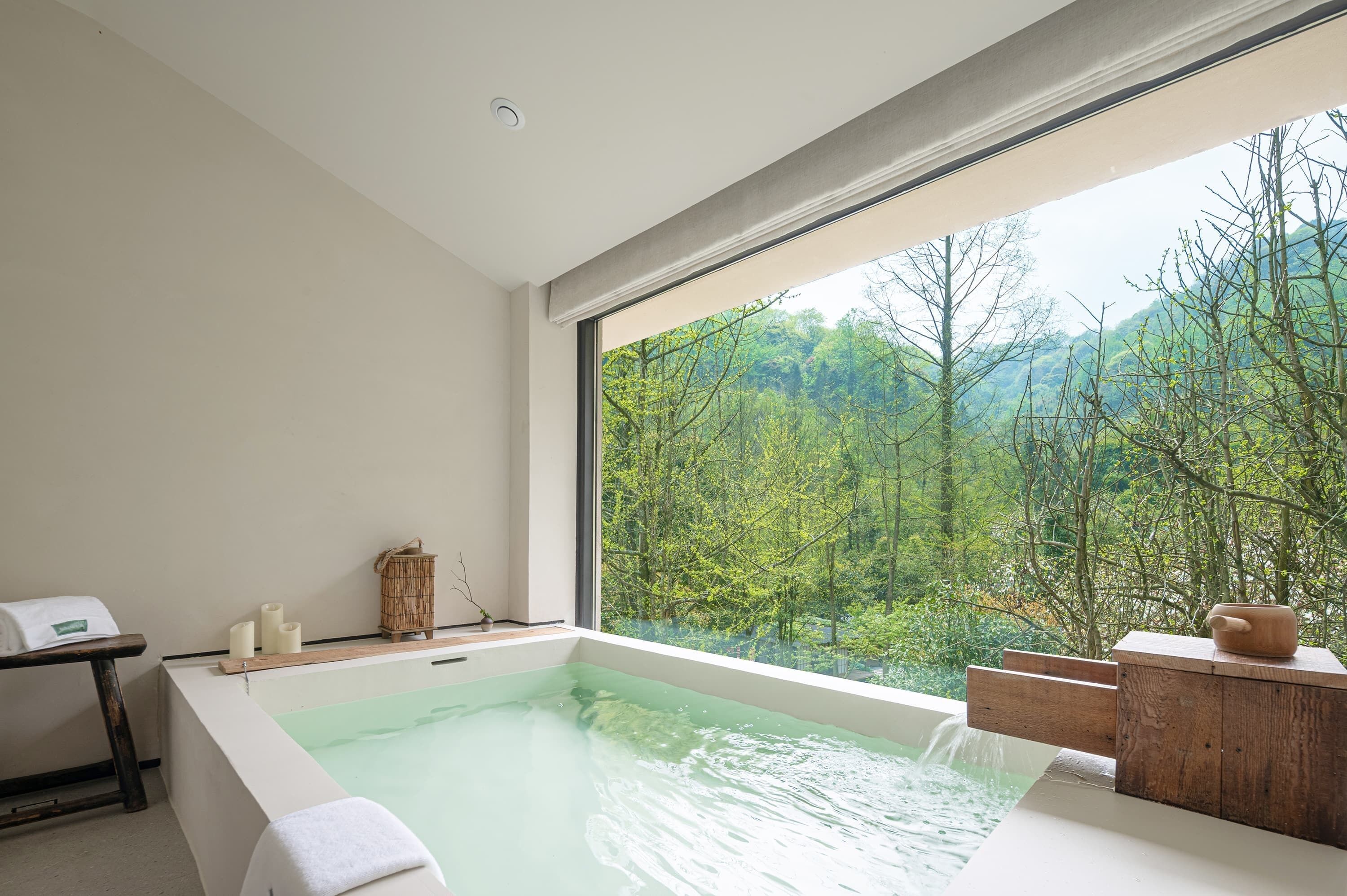 Un baño moderno con un ventanal grande, una bañera y una mesita de madera.