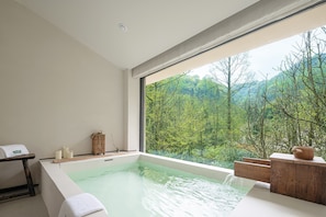 Un bagno moderno con una grande finestra, una vasca da bagno e un tavolino di legno.