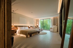 Ein modernes Schlafzimmer mit einem großen Bett, Nachttischen, einem Sessel und Blick auf Grün hinter großen Fenstern.
