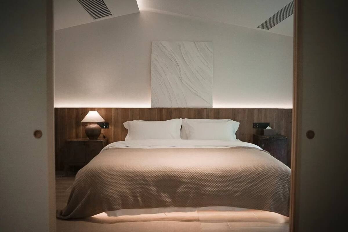 A modern bedroom with a bed, a nightstand, a lamp, and a wall-mounted artwork.