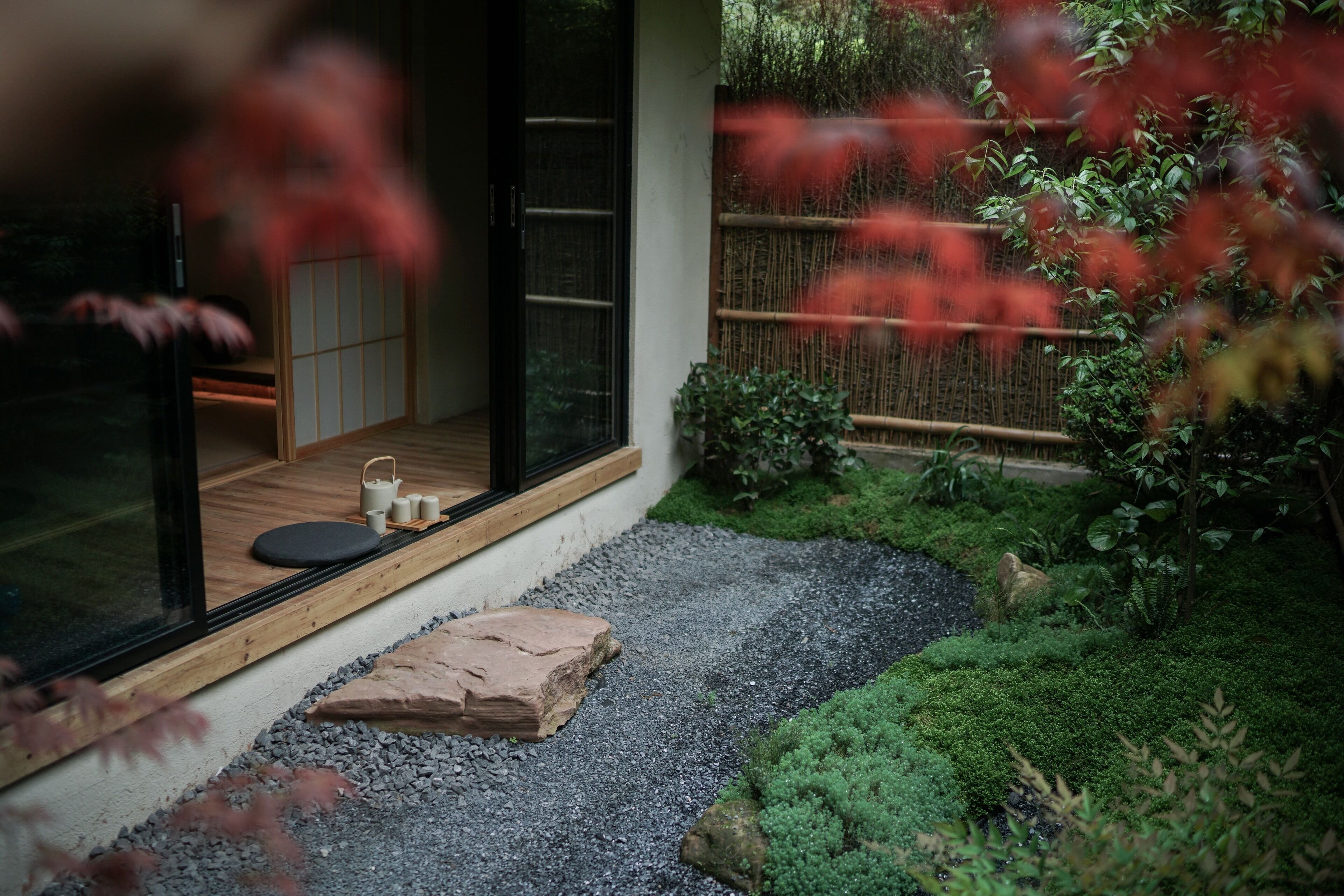 A traditional Japanese-style room with tatami flooring, a sliding door, and a small garden area with a gravel path, rocks, and greenery.