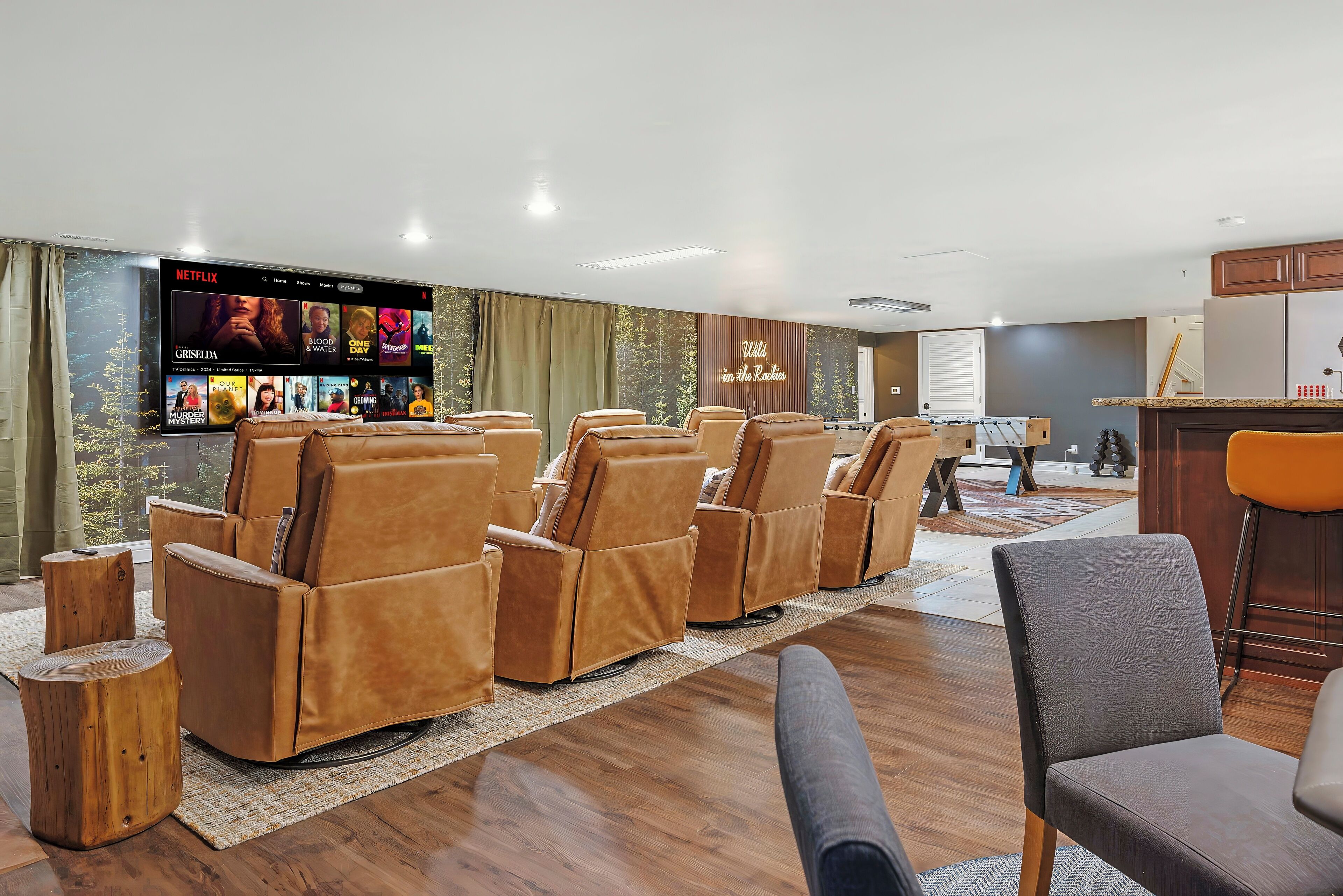 A modern living room with leather recliners, a flat-screen TV displaying Netflix, and a kitchen area in the background.