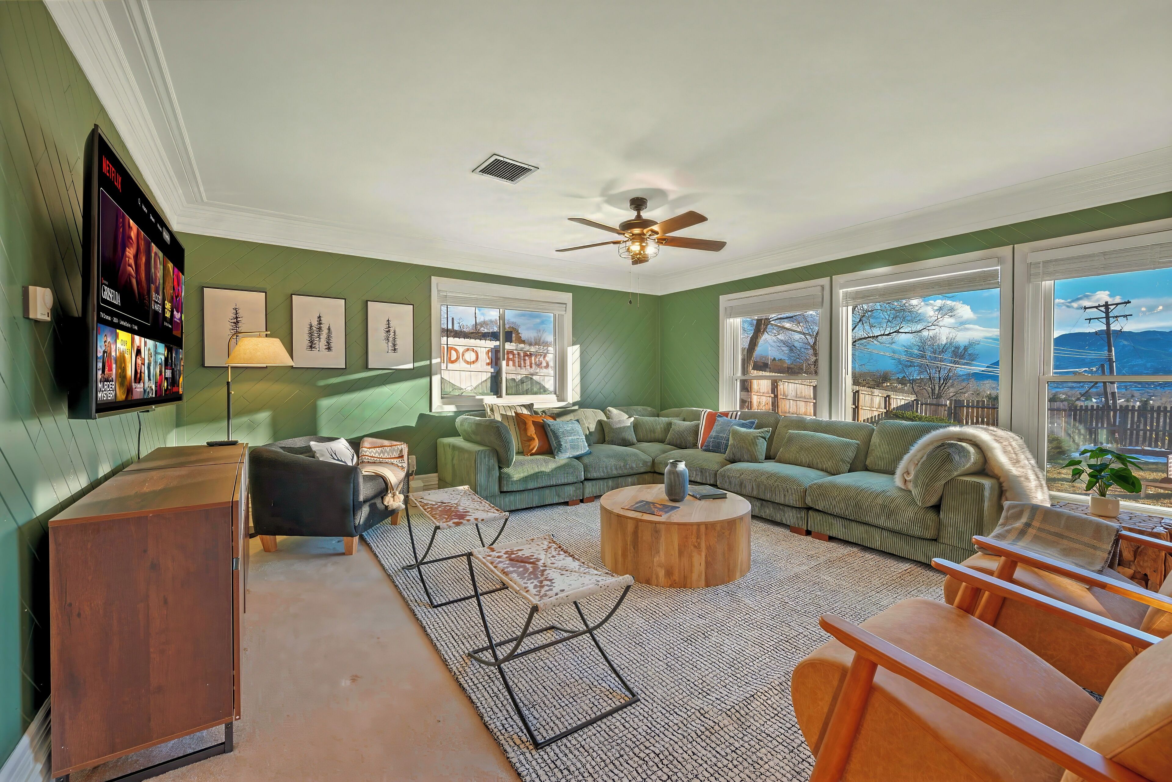 A living room with a green couch, a wooden coffee table, and a TV mounted on the wall.