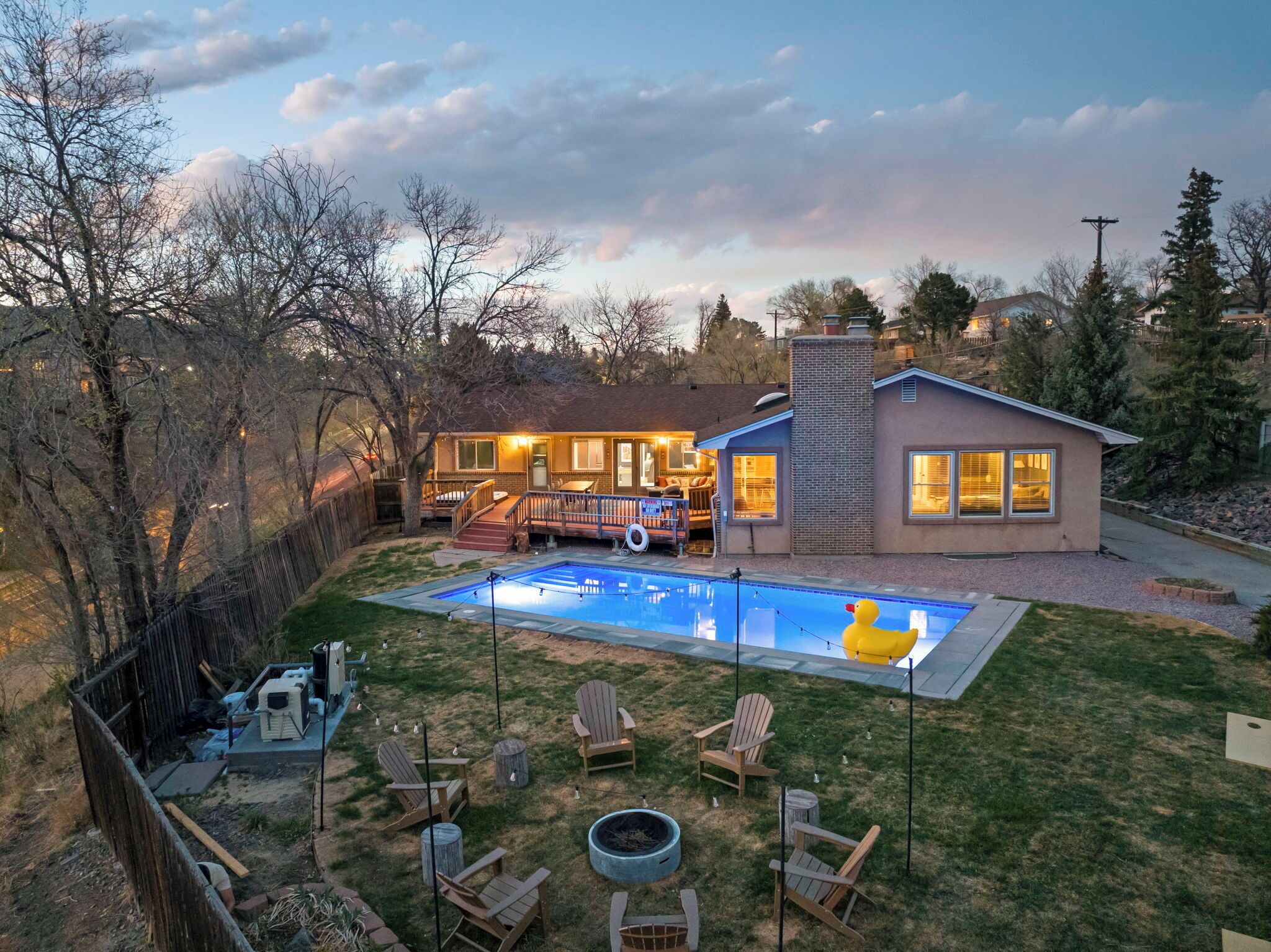 Un patio trasero con piscina, terraza de madera y mobiliario exterior.