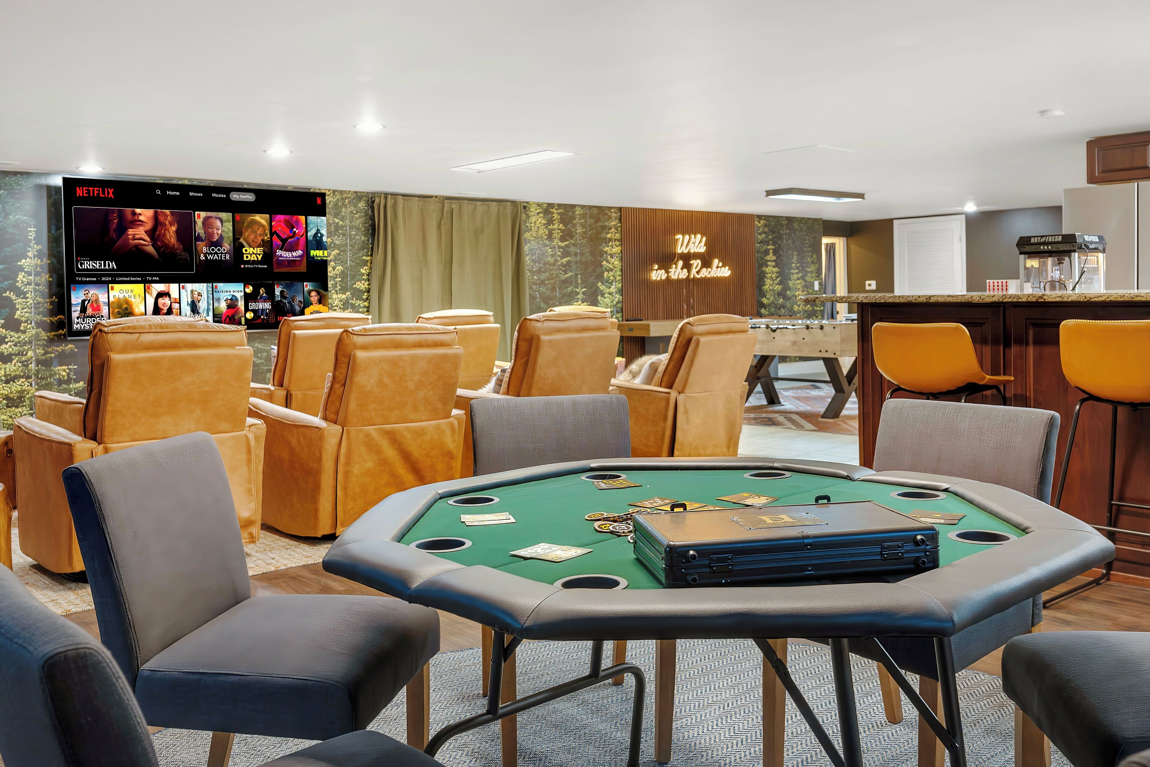 A casino area with a green felt table, poker chips, and cards. There are multiple chairs around the table. A large screen displays a Netflix interface with various shows and movies. The room has a wooden bar and a sign that reads "Wild in the Rockies."